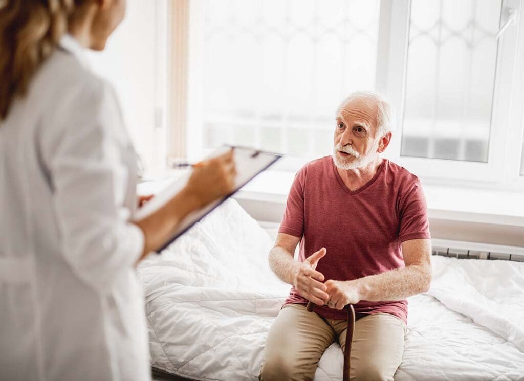 Hospital Indemnity Plans - Senior Male Patient with Cane Talking about His Health with a Female Physician Who is Taking Notes