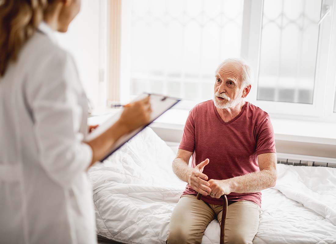 Hospital Indemnity Plans - Senior Male Patient with Cane Talking about His Health with a Female Physician Who is Taking Notes